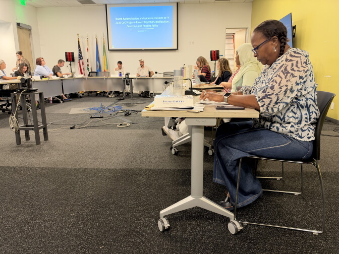 A woman sites at the end of a long desk beside more than a dozen others, reviewing documents. 