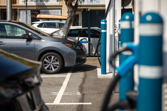 A gray sedan is connected to a charger at an electric vehicle charging station. 