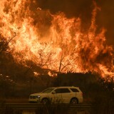 Vehicles pass beside a wall of flames on the 101 highway as it reaches the coast during the Thomas wildfire near Ventura, California on December 6, 2017. California motorists commuted past a blazing inferno Wednesday as wind-whipped wildfires raged across the Los Angeles region, with flames triggering the closure of a major freeway and mandatory evacuations in an area dotted with mansions. / AFP PHOTO / MARK RALSTON (Photo credit should read MARK RALSTON/AFP/Getty Images)