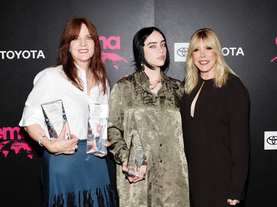 Three light-skinned women with shoulder length hair stand next to each other, holding awards and posing for a photo.  There is a black background with logos like "Toyota" on it.