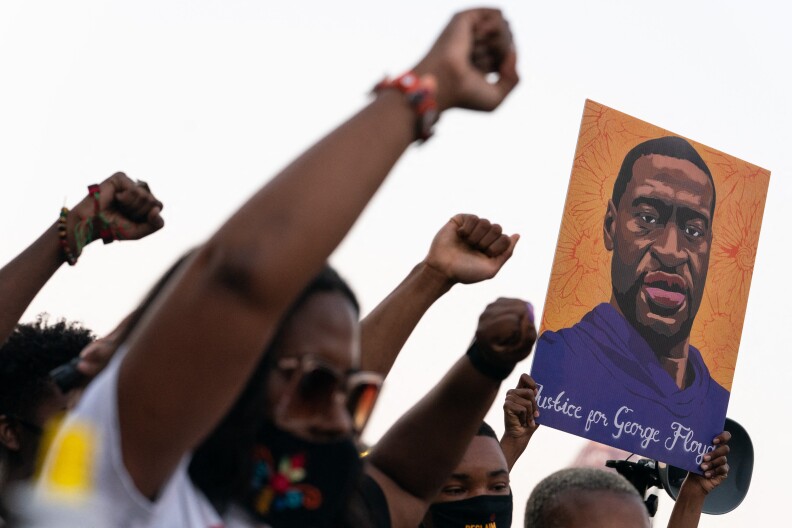 People march with their right arms raced as they carry a painting of George Floyd.