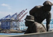 Cranes stand at a port. In the foreground is a statue from the Terminal Island Japanese Fishing Village Memorial.