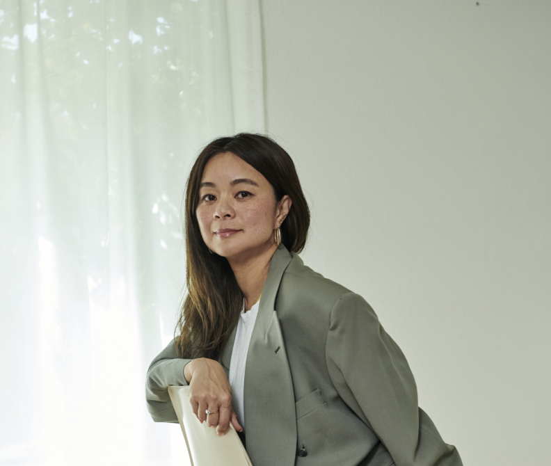 An Asian American woman with long hair and wearing a gray blazer poses for the camera.