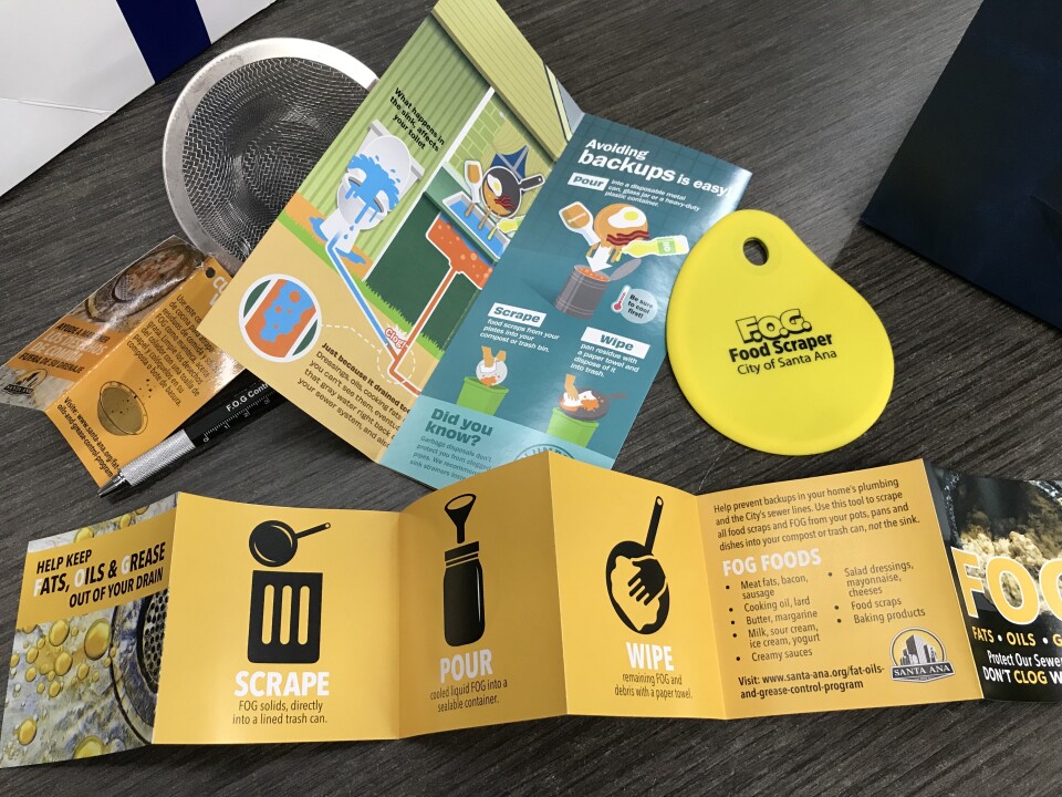 Spread out on a table: A brochure with separate pages that say "SCRAPE, POUR, WIPE" with graphics; a yellow food scraper, another brochure on avoiding sewer backups and a sink strainer. 