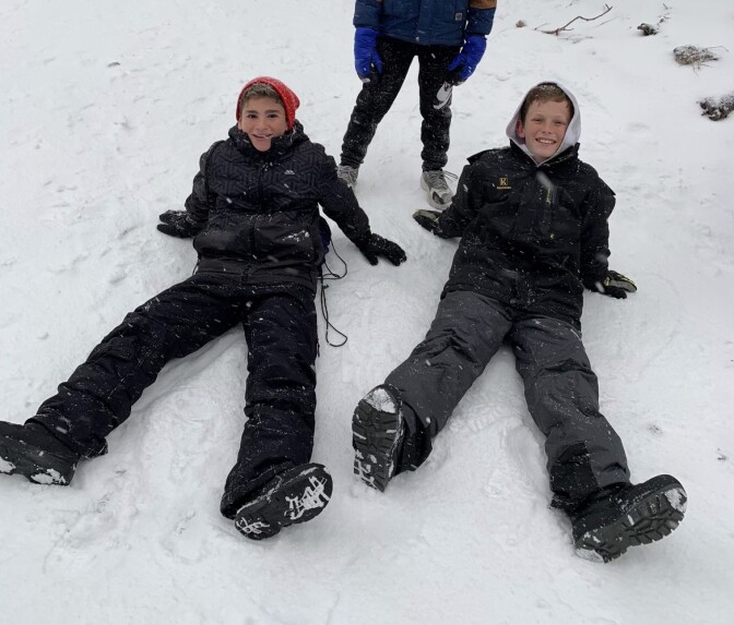 Photo of two middle school-aged boys in winterwear smiling and making snow angels.