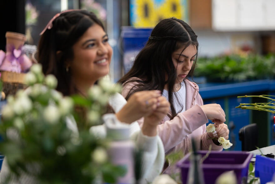 Two teenage girls, each with light brown skin, put together flower decorations.
