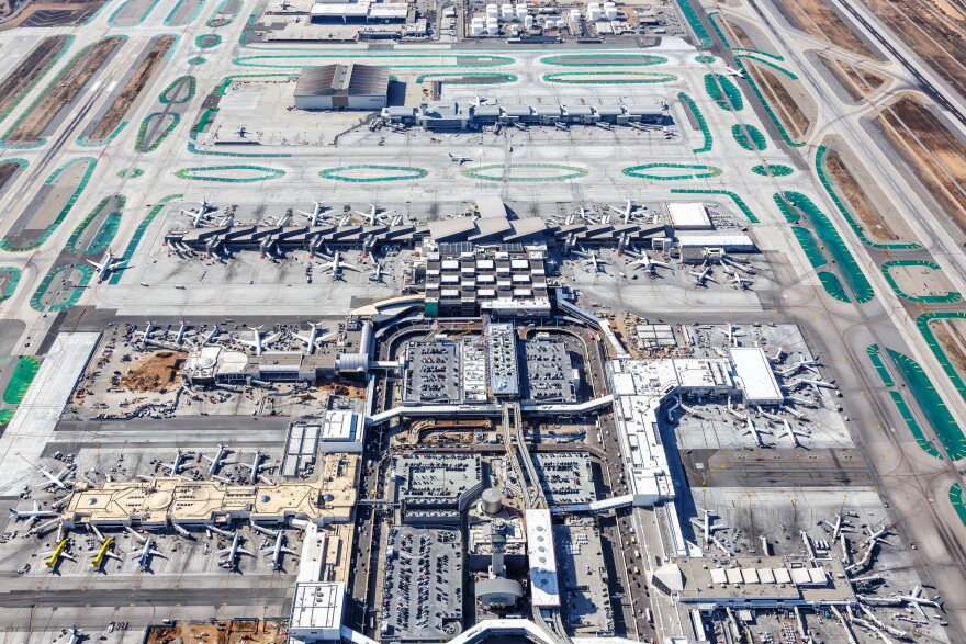A aerial view shows a large airport with multiple wings and planes parked at gates