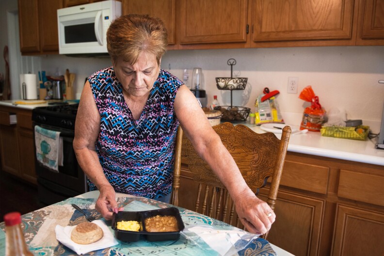 A woman stands over a plate of food at her dining table.