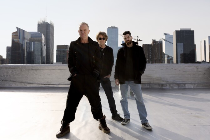 Sting and two more musicians stand on a rooftop, posed for the camera.