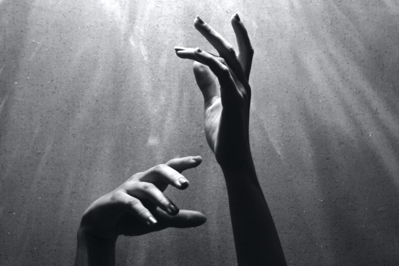 A black-and-white photo of two hands in motion, sunlit from above.