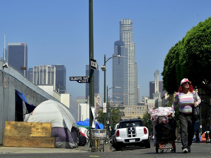 A woman pushes her cart full of belongings along the street past tents on the sidewalk near Skid Row in downtown Los Angeles, California on June 20, 2017.