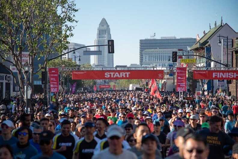 Firecracker L.A. Run starting line with hundreds of people running. LA City Hall can be seen in the distance.