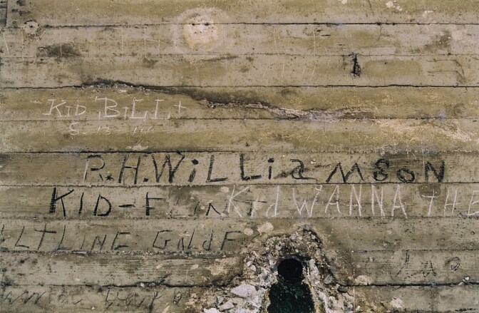 A close look at a bridge underpass, with specific focus on a set of old marking, writings that trace back to the 1900s.