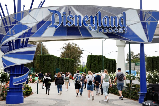 People walk under a blue and white sign that reads Disneyland Resort.
