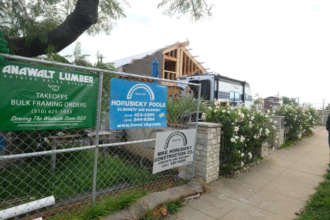 Fencing lines a sidewalk next to a home under construction. Signs on the fence bear the Horusicky name.