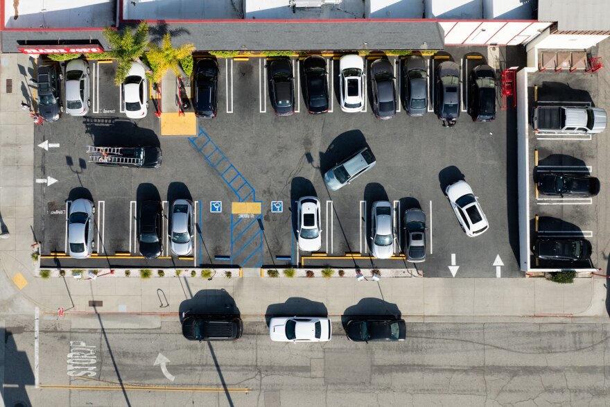 An aerial view of a cramped, packed paved parking lot, with cars filling almost every space.