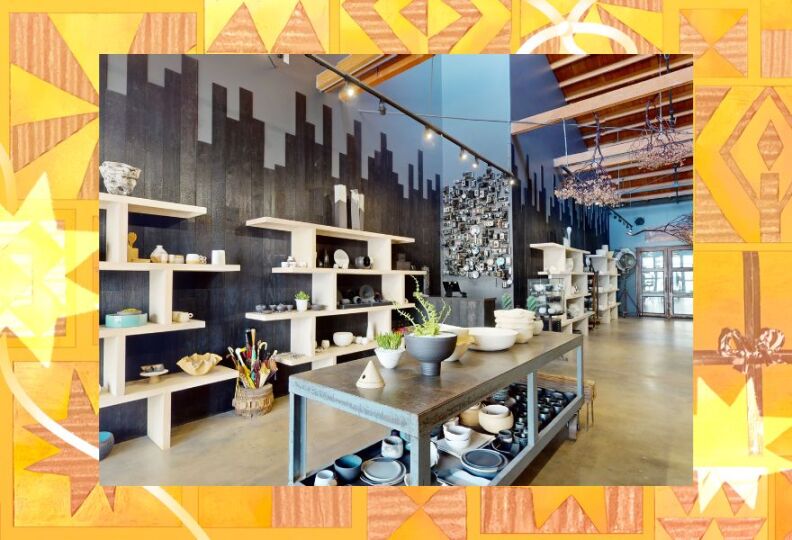 The interior of a store: There is a large gray table in the middle of the floor and it is holding pottery of various shapes and colors and designs, mainly cups, bowls and vases. The walls are also lined with shelving holding similar items. The photo is set against a festive gold background accented with images of stars, gift boxes and ribbons.