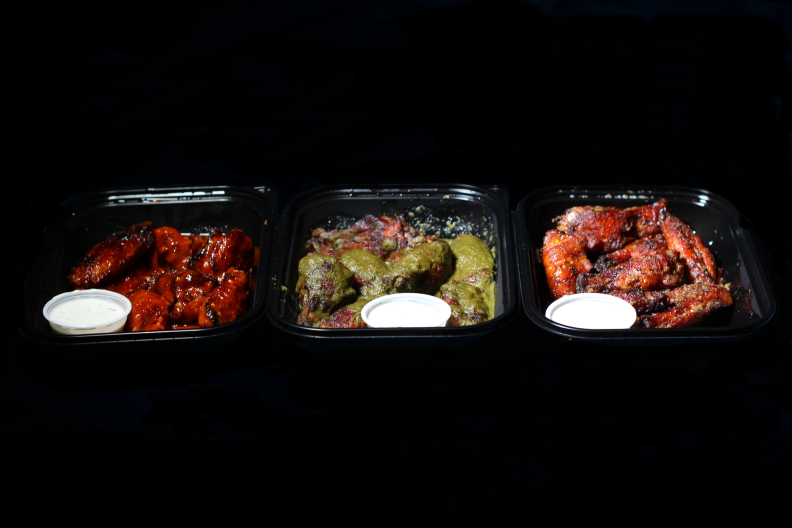 Three plastic takeout containers are filled with chicken wings