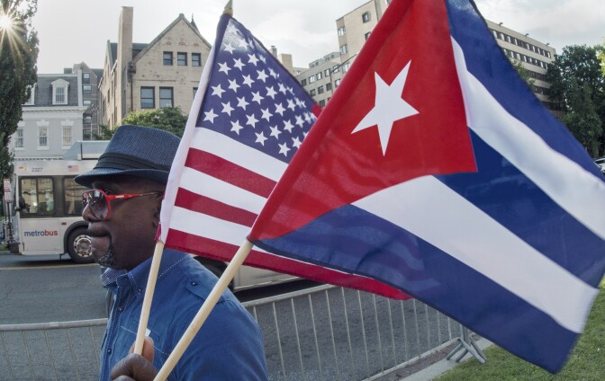 A man waves the US and Cuban flags as he walks in front of the new Cuban Embassy shortly before it's official ceremonial opening July 20, 2015, in Washington, DC. The United States and Cuba formally resumed diplomatic relations on July 20, as the Cuban flag was raised at the US State Department in a historic gesture toward ending decades of hostility between the Cold War foes.   AFP PHOTO/Paul J. Richards        (Photo credit should read PAUL J. RICHARDS/AFP/Getty Images)