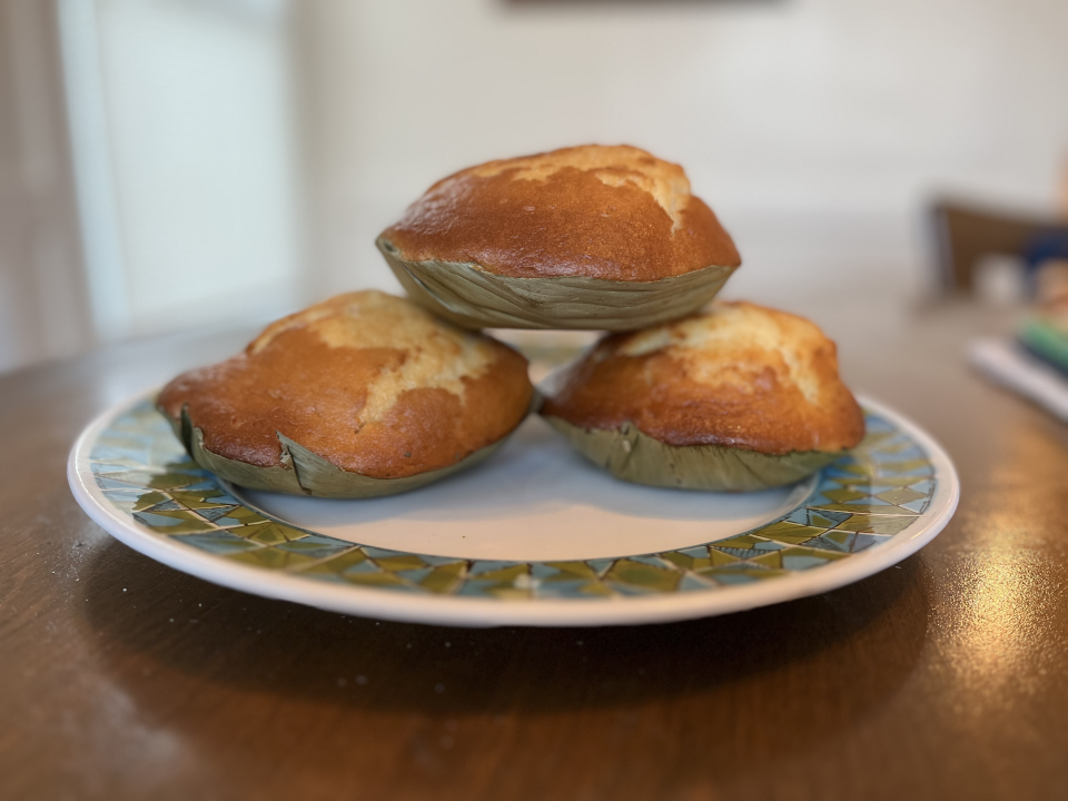Three dessert breads sit on a white plate with a green and blue design on a brown table top 