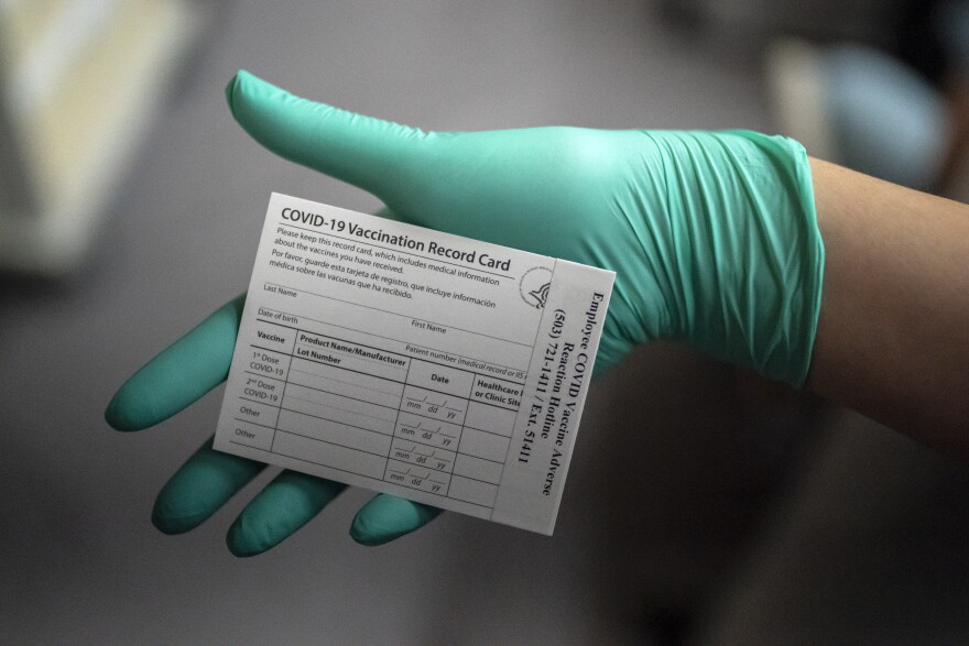A person in a green plastic glove holds a blank COVID-19 vaccination record card.