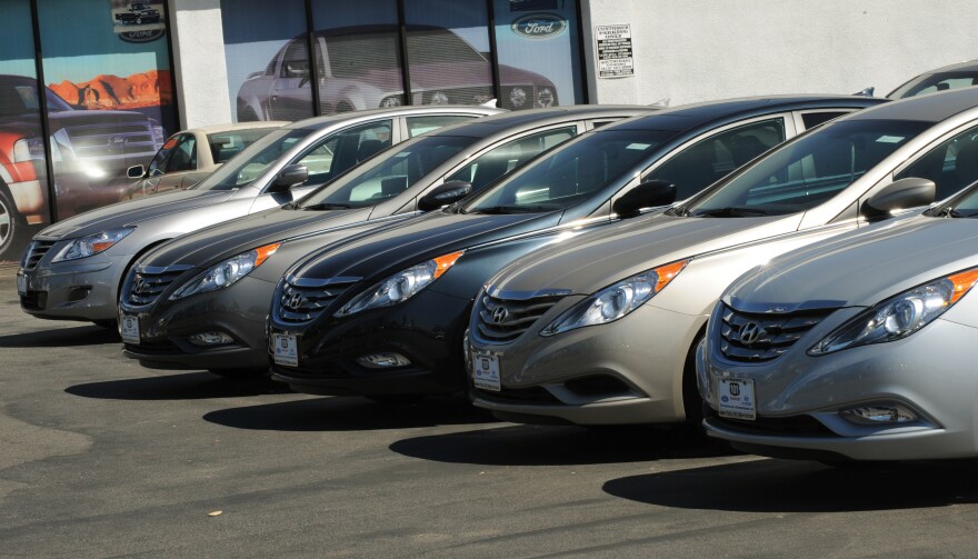 A row of sedans with the Hundai logo on the grill are in a row in a dealership parking lot.