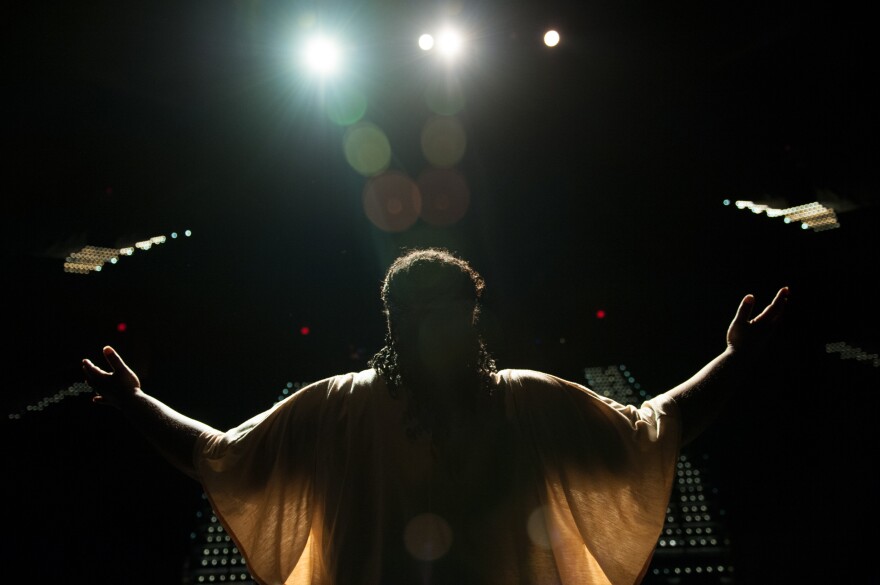 A person with arms outstretched on a dark stage in shadows