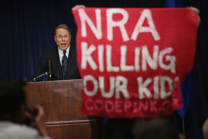 A demonstrator from CodePink holds up a banner as National Rifle Association Executive Vice President Wayne LaPierre delivers remarks during a news conference at the Willard Hotel December 21, 2012 in Washington, DC. This is the first public appearance that leaders of the gun rights group have made since a 20-year-old man used a popular assault-style rifle to slaughter 20 school children and six adults at Sandy Hook Elementary School in Newtown, Connecticut, one week ago. 