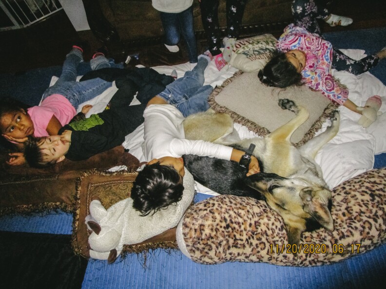 In this image, four children lay on the floor with blankets, pillows, and a dog.