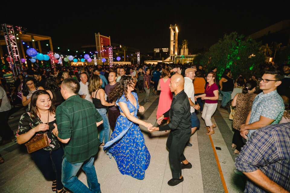 A crowd of people dancing on the Music Center Plaza at night
