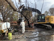 A worker sprays down debris before a claw truck picks it up at a home burned down in the Woolsey Fire in Malibu. 