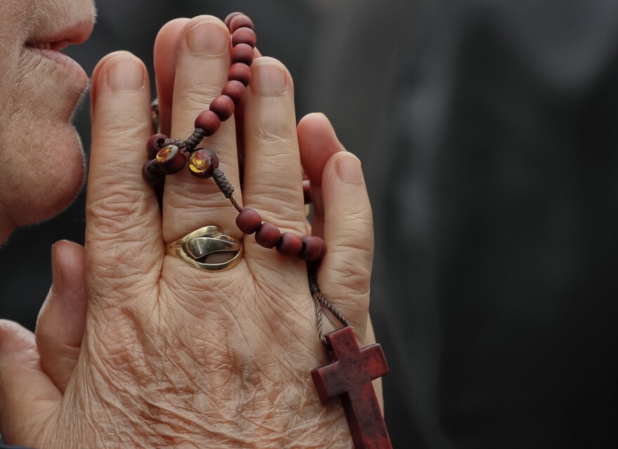 In this Sunday, Oct. 23, 2016 picture a Catholic worshiper prays during a pilgrimage with Pope John Paul II's remains, in Bucharest, Romania. Both churches parade holy remains. The Catholics have a few drops of the blood of Saint John Paul II; the Orthodox claim to have the remains of three saints including those of St. Dimitrie, the patron saint of Bucharest. (AP Photo/Vadim Ghirda)