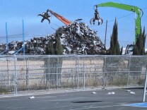Two industrial waste machines can be seen from the blacktop at Jordan High School in Watts. Two massive claws hover over large piles of metal waste. 