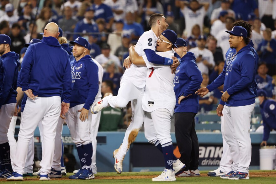 An image of Dodger players celebrating a win. Two players in uniform embrace in a hug as others are around them.