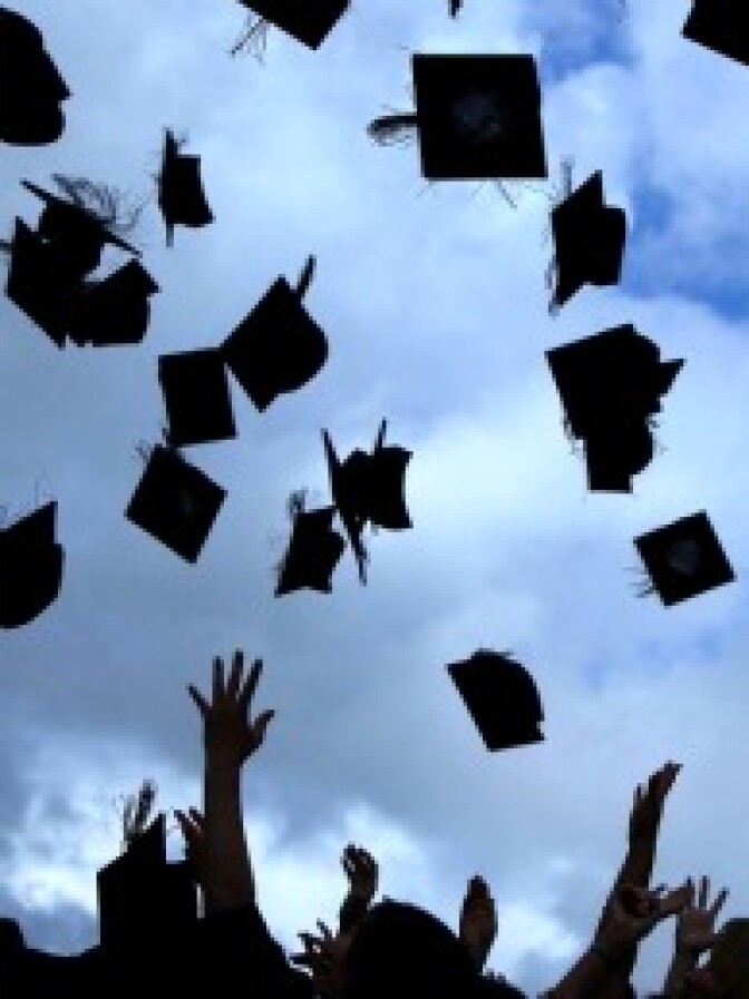 Students throw their mortarboards in the air during their college graduation.