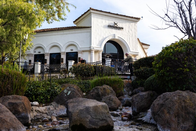 A large white building with a sign that reads "Crossroads." In the foreground there's a water fountain/creek with rocks.