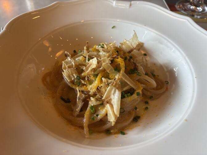 A spaghetti dish topped with bonito flakes, light papery shavings of dried fish common in Japanese cuisine, and shaved bottarga, cured fish roe in the form of orange powdery flakes, topped with chopped chives. 