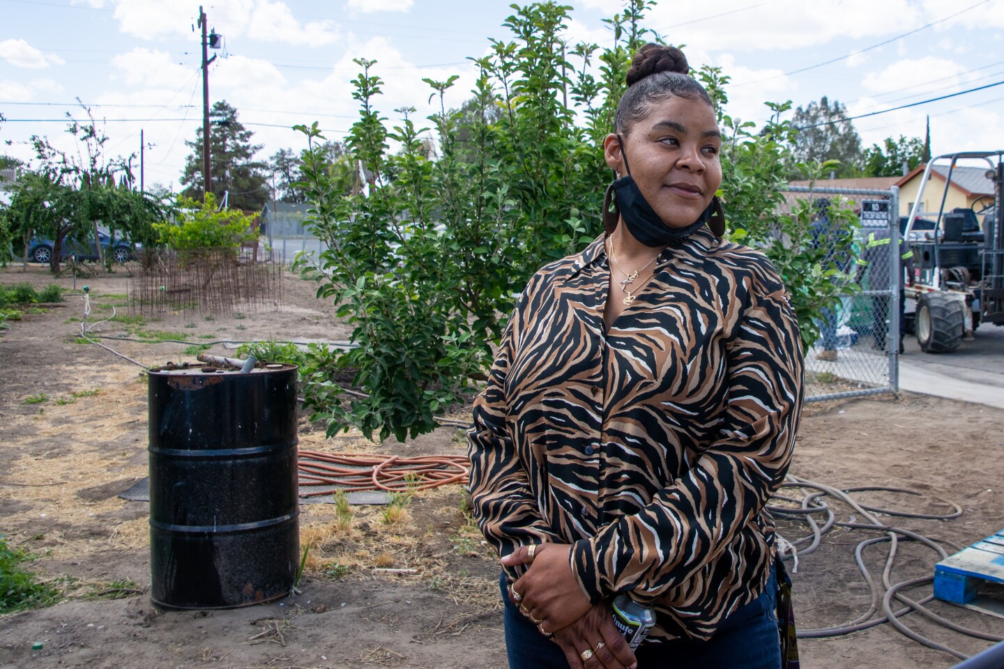 Christina Crompton, standing in a vacant lot, wears an animal print blouse, with arms crossed and a mask under her chin.