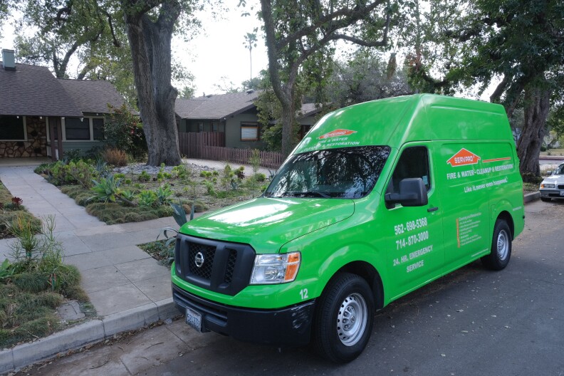 A bright green smoke remediation van is parked on a residential street in Pasadena, a few blocks away from where homes burned down in the Eaton Fire. 