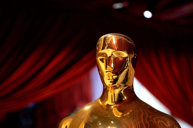 A gold Oscar statue is seen up close with red drapes behind it