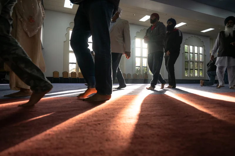 A photo taken inside as people walk on the floor. They are wearing long pants and are barefoot.