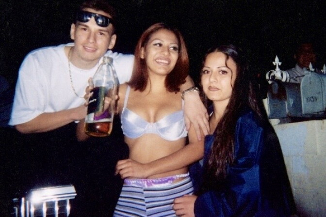 Three young people stand next to each other, the male presenting person wears a white t-shirt. The two female presenting people have long, dark hair.