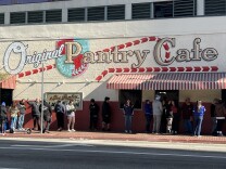 People stand in line under a mural reading: Original Pantry Cafe