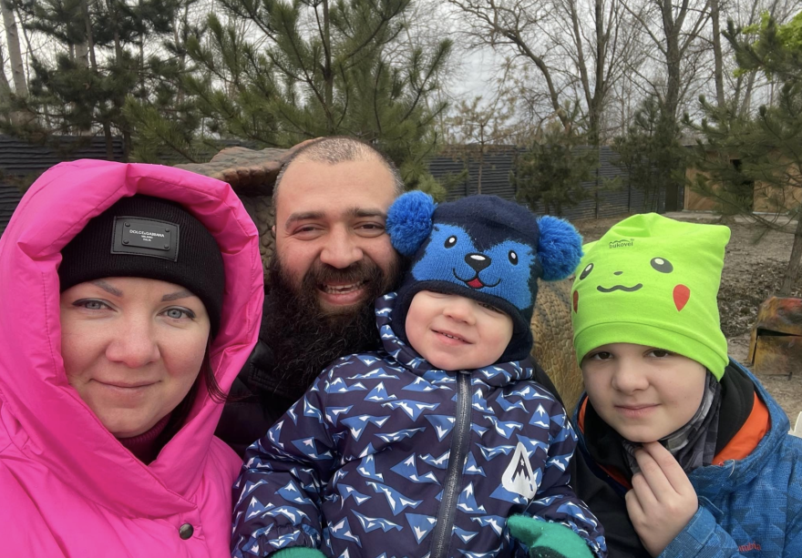 Left to right: A woman in a pink hooded jacket, a man with a beard wearing black, a toddler in a blue jacket and animal-face hat and a child in a yellow Pokemon beanie.