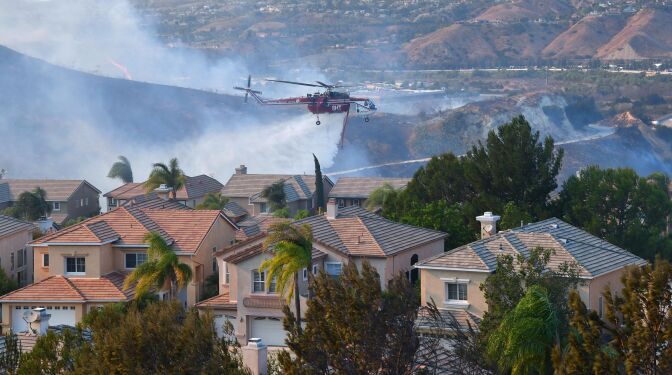 A helicopter drops water near homes at the Anaheim Hills neighborhood in Anaheim on Oct. 9, 2017, after a fire spread quickly through the area prompting mandatory evacuations and freeway closures.