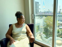 Lisa Chilton wears a flower sun dress while sitting in a chair in her living room while looking out the window.