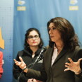 A woman speaks at a podium as two women look on from behind.