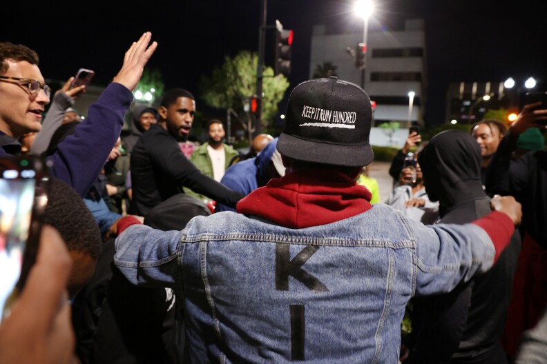A crowd of people with various skin tones surrounds a man with a hat that says "Keep It Run Hundred".