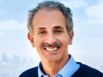 Headshot of Mike Feuer. He's smiling and wearing a blue collared shirt and dark sweater or jacket. He has gray wavy hair and a mustache and a light complexion.