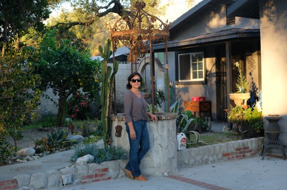 A woman stands next to a well in the yard of a home.